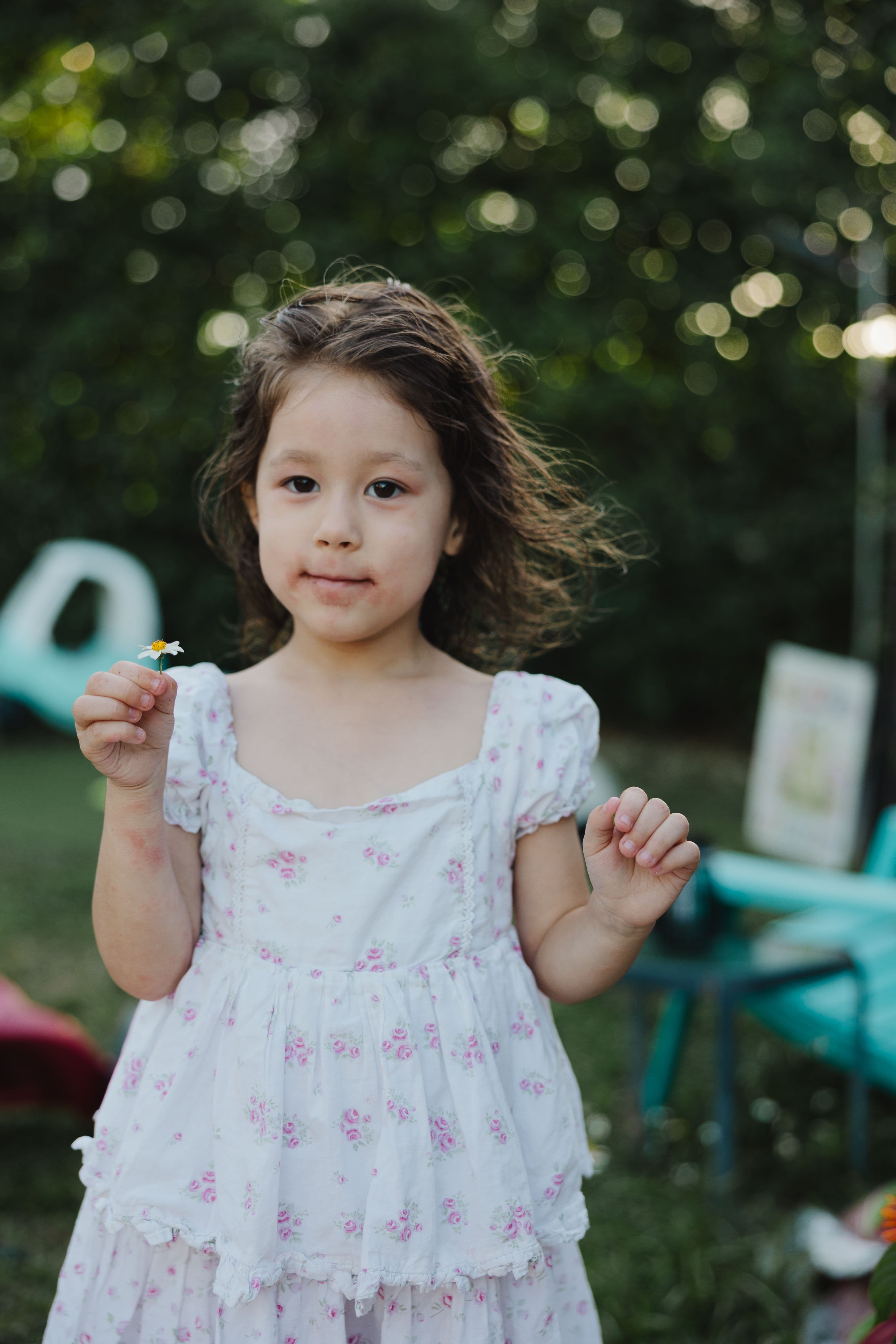 Daughter in floral dress holding a daisy in the backyard, golden hour South Florida family photography.
