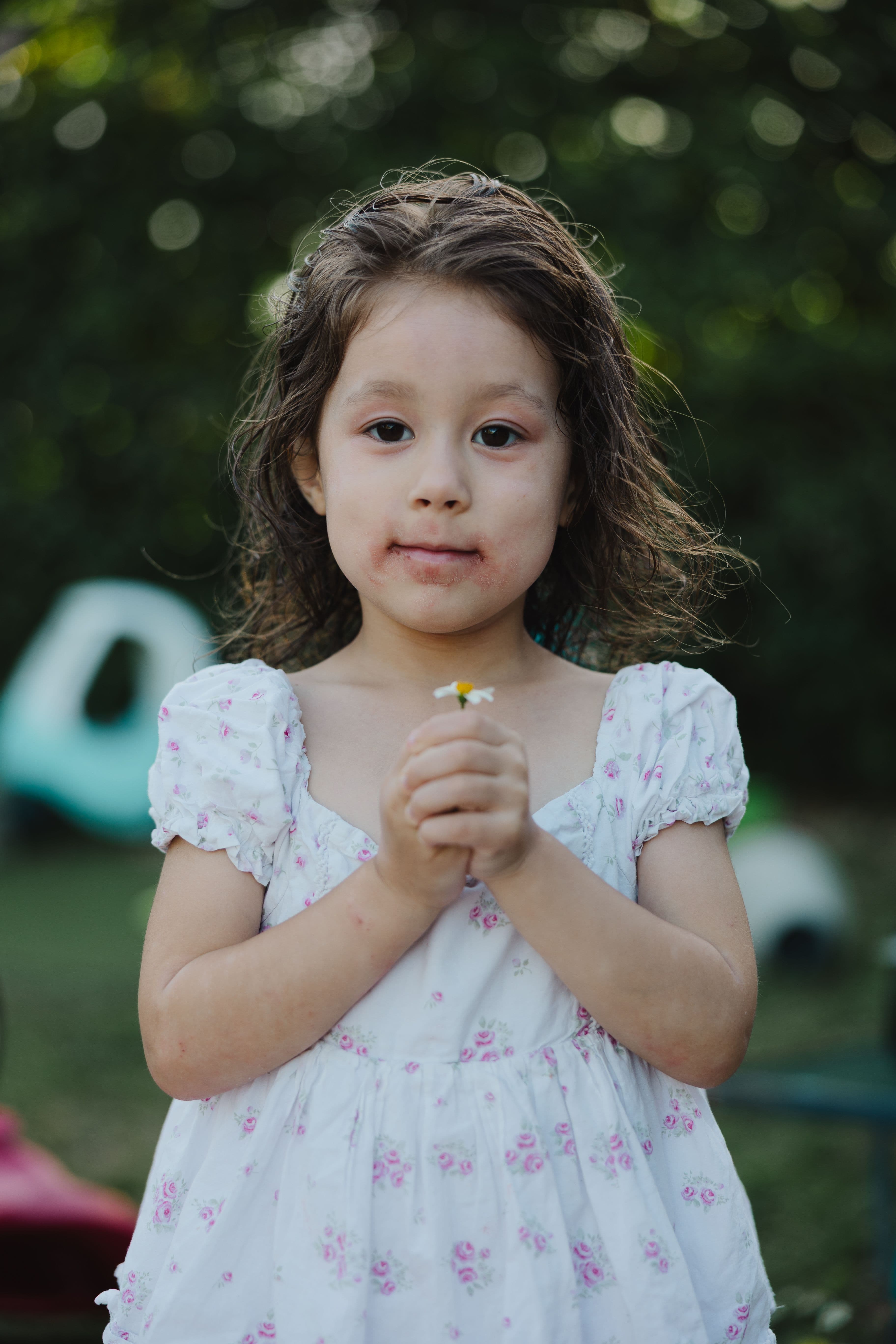 Girl in floral dress holding a daisy with both hands, honest unedited family portrait in Fort Lauderdale.