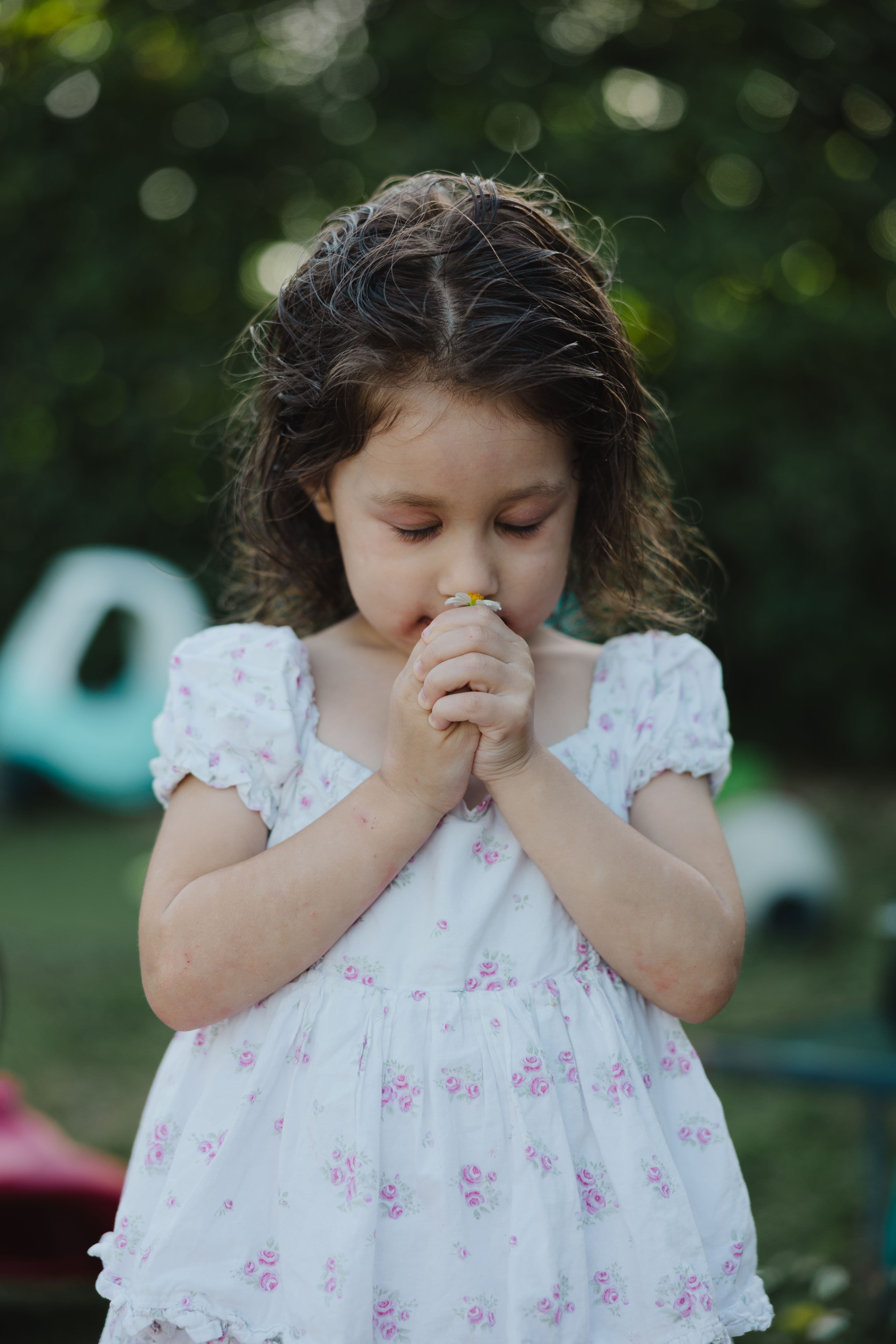 Young daughter in floral dress smelling a small daisy in the backyard, captured by Fort Lauderdale family photographer Little Chapters.
